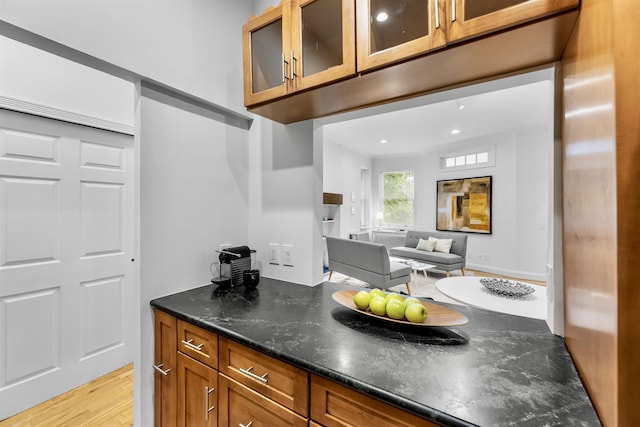 264 9th St Unit 2R, Jersey City, NJ 07302 - kitchen with brown cabinets, glass insert cabinets, light wood-style flooring, dark stone countertops, and open floor plan