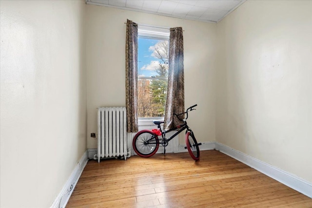 unfurnished room featuring radiator heating unit, baseboards, and light wood finished floors