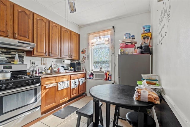 kitchen with brown cabinetry, light countertops, under cabinet range hood, appliances with stainless steel finishes, and backsplash