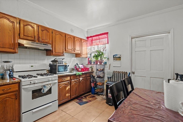 kitchen with under cabinet range hood, stainless steel microwave, tasteful backsplash, crown molding, and white gas range