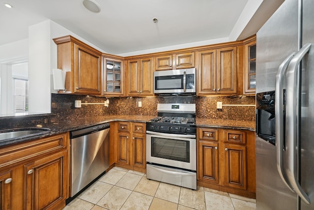 45 Broadway Unit 204, Jersey City, NJ 07306 - kitchen featuring stainless steel appliances, brown cabinets, dark stone countertops, decorative backsplash, and glass insert cabinets