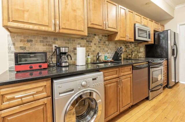 kitchen featuring light wood-style flooring, appliances with stainless steel finishes, ornamental molding, a sink, and washer / dryer