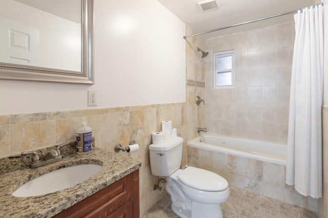 full bath featuring toilet, vanity, visible vents, tiled shower / bath, and tile walls