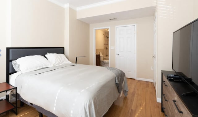 bedroom featuring light wood finished floors, visible vents, ornamental molding, ensuite bath, and baseboards