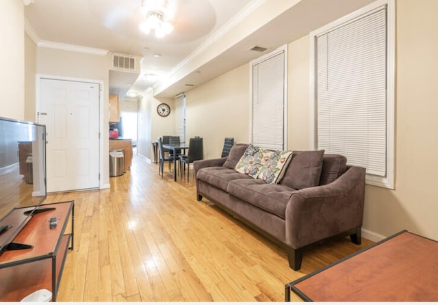 living area with baseboards, light wood-style flooring, visible vents, and crown molding