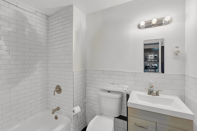 full bathroom featuring toilet, tiled shower / bath combo, vanity, and tile walls