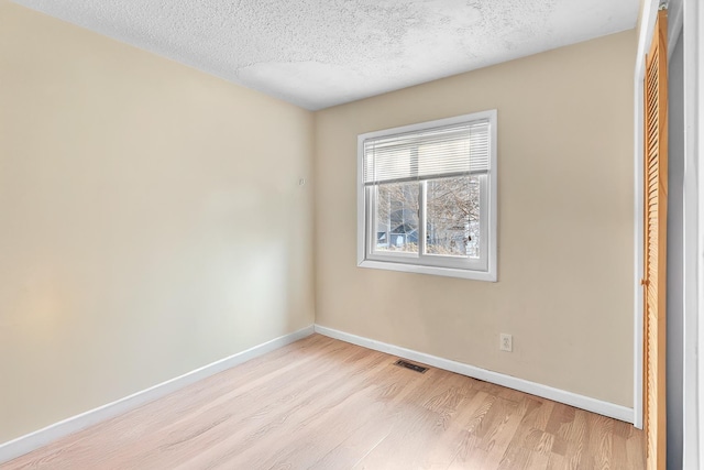 empty room featuring light wood-style flooring, baseboards, visible vents, and a textured ceiling