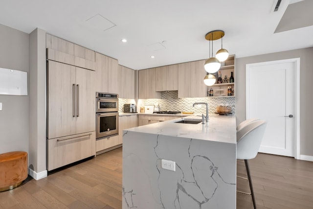 kitchen featuring a kitchen breakfast bar, modern cabinets, appliances with stainless steel finishes, a sink, and light brown cabinetry