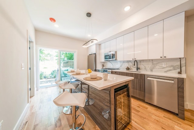 kitchen with white cabinetry, appliances with stainless steel finishes, light wood-type flooring, pendant lighting, and sink