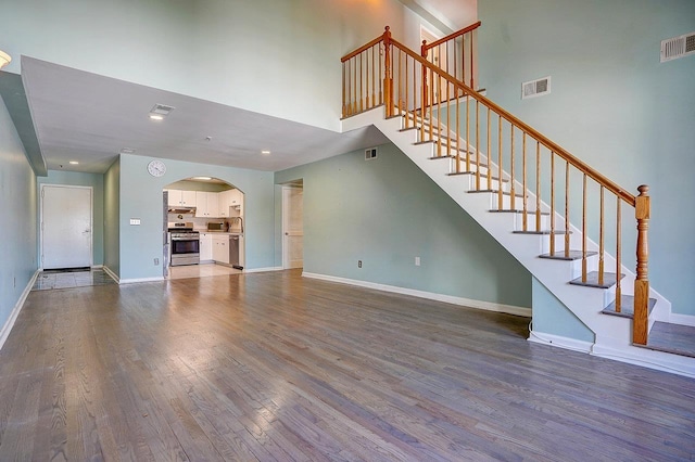 54 Polk St, Newark, NJ 07105 - unfurnished living room with arched walkways, dark wood-type flooring, a towering ceiling, and stairway