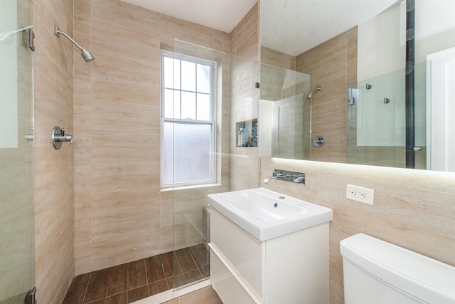 bathroom with vanity, a tile shower, tile walls, and toilet