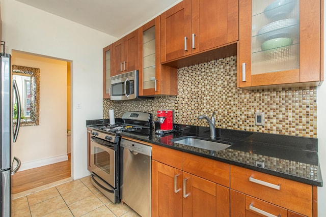 kitchen with sink, light tile patterned floors, appliances with stainless steel finishes, dark stone countertops, and tasteful backsplash