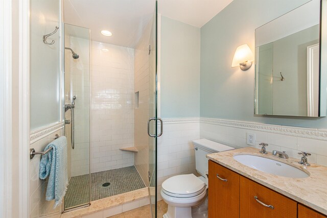 bathroom with vanity, a stall shower, wainscoting, tile walls, and toilet