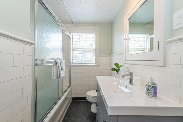 full bath with toilet, tile walls, wainscoting, bath / shower combo with glass door, and vanity