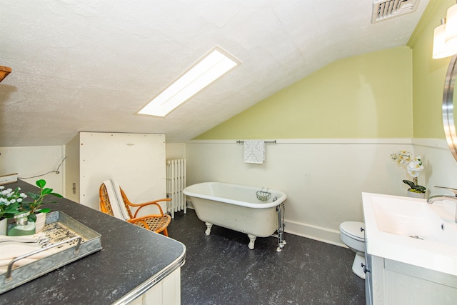 bathroom featuring visible vents, lofted ceiling with skylight, a freestanding bath, radiator heating unit, and a textured ceiling