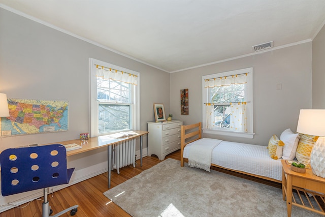 bedroom featuring radiator heating unit, multiple windows, wood finished floors, and visible vents