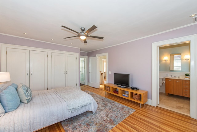 bedroom featuring light wood finished floors, ensuite bath, crown molding, and a ceiling fan