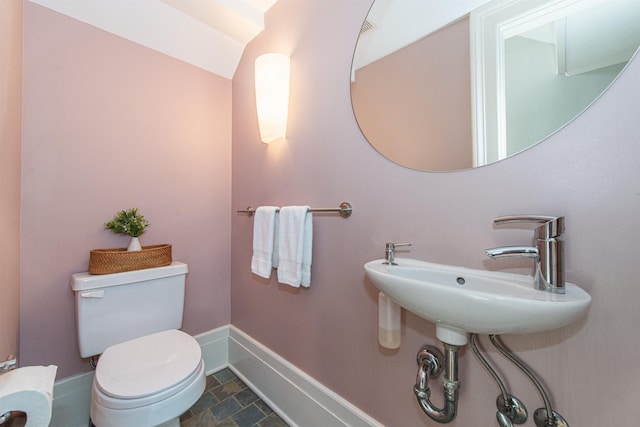 half bathroom featuring toilet, baseboards, and stone finish flooring