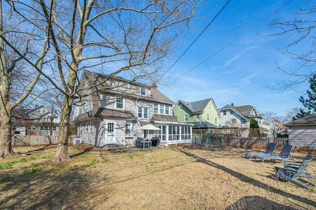 rear view of property with central AC unit, fence, a yard, a sunroom, and a chimney