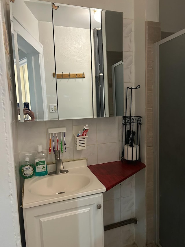 bathroom with a shower with door, vanity, and backsplash