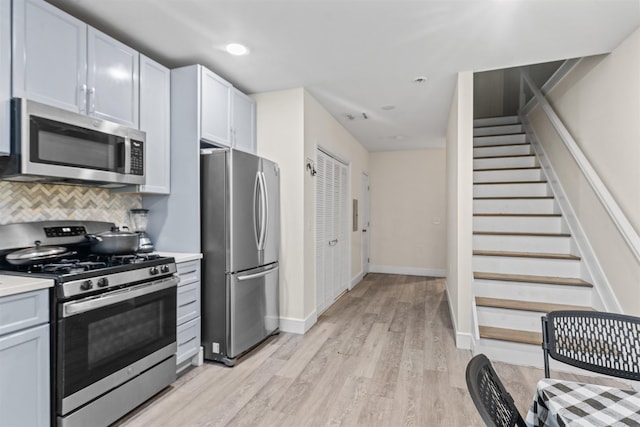 kitchen with tasteful backsplash, baseboards, light wood-type flooring, light countertops, and appliances with stainless steel finishes