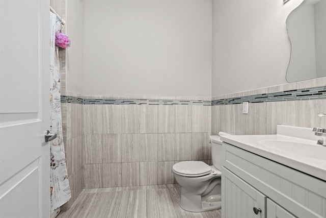 full bath with a wainscoted wall, toilet, a shower with shower curtain, vanity, and tile walls