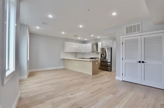 443 Bergen Ave Unit 3, Jersey City, NJ 07304 - kitchen with stainless steel fridge, a peninsula, white cabinets, wall chimney exhaust hood, and light wood-type flooring