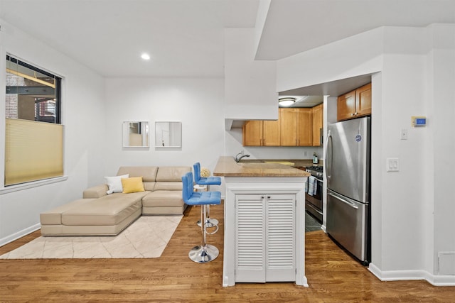 kitchen featuring light wood finished floors, a breakfast bar, a peninsula, stainless steel appliances, and open floor plan