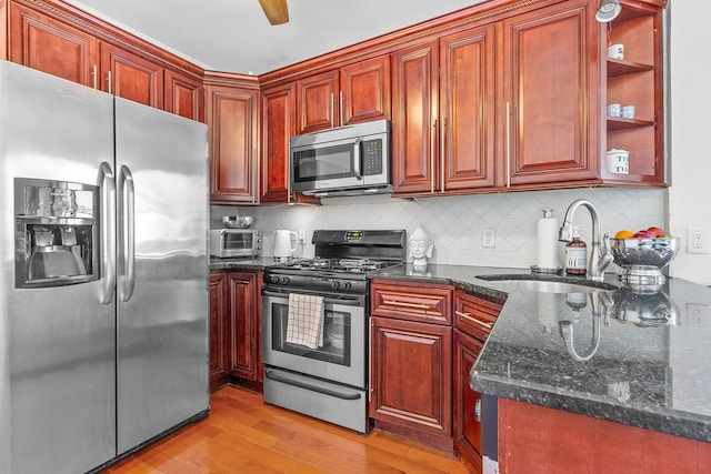 kitchen featuring backsplash, dark stone counters, appliances with stainless steel finishes, light wood-style floors, and a sink