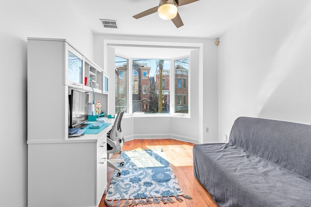 office area with light wood-style floors, a ceiling fan, visible vents, and baseboards