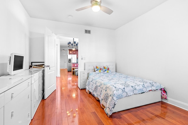 bedroom with visible vents, light wood-style floors, stainless steel fridge with ice dispenser, and ceiling fan with notable chandelier