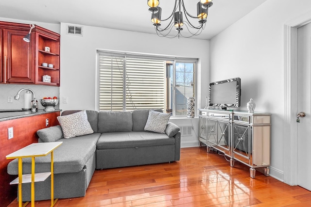 living room featuring visible vents, baseboards, a notable chandelier, and light wood finished floors