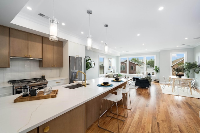 kitchen featuring light stone counters, stainless steel appliances, crown molding, sink, and decorative light fixtures