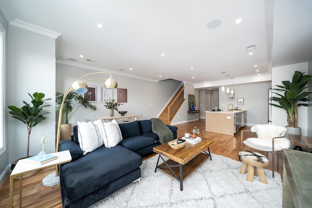 living room with ornamental molding, sink, and light hardwood / wood-style flooring