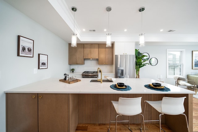 kitchen with sink, hanging light fixtures, light stone countertops, ornamental molding, and stainless steel appliances