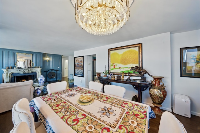 dining space featuring a warm lit fireplace, baseboards, wood finished floors, and an inviting chandelier