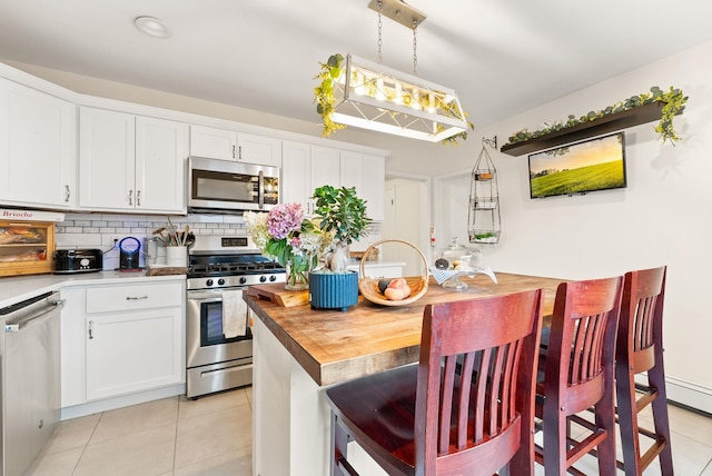 26 E 49th St, Bayonne, NJ 07002 - kitchen featuring stainless steel appliances, light tile patterned floors, wooden counters, tasteful backsplash, and white cabinets