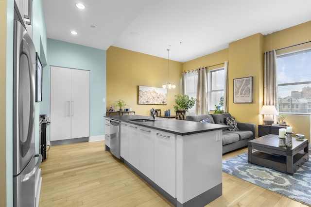 kitchen featuring white cabinets, dark countertops, light wood-style flooring, appliances with stainless steel finishes, and a sink