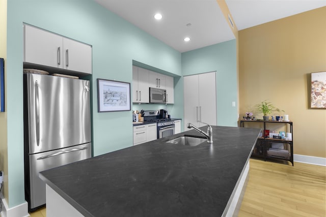 kitchen featuring a center island with sink, dark countertops, light wood-style flooring, stainless steel appliances, and a sink