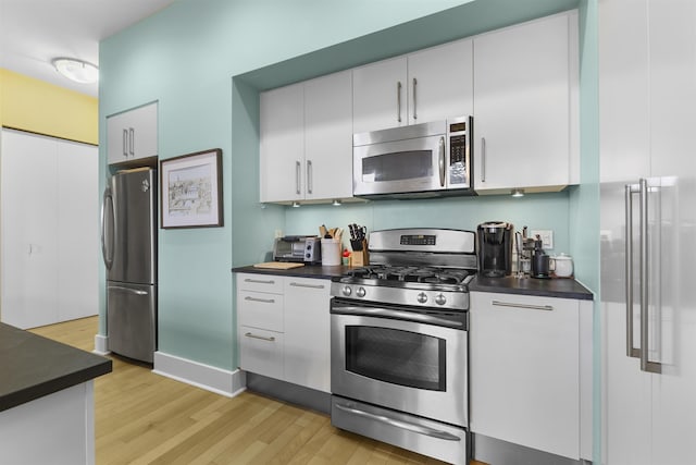 kitchen featuring dark countertops, light wood finished floors, white cabinets, and stainless steel appliances