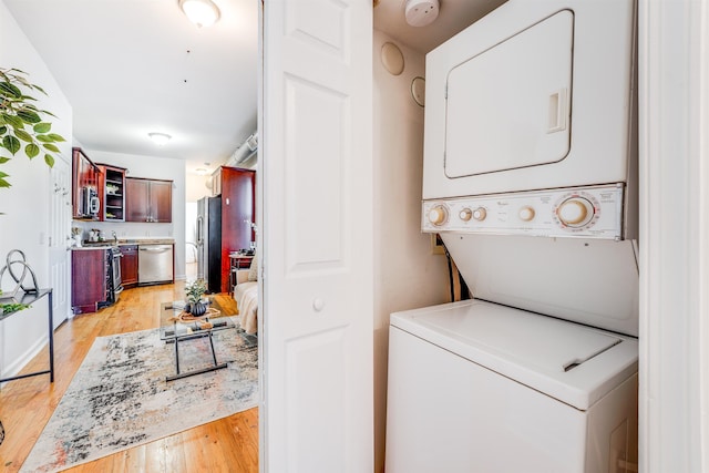 laundry area featuring stacked washer and dryer and light hardwood / wood-style flooring