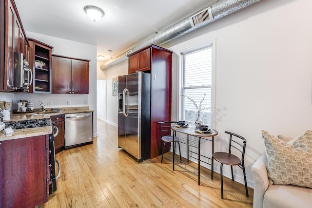 kitchen with stainless steel appliances, light hardwood / wood-style flooring, and light stone countertops