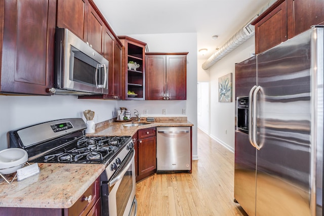 kitchen with sink, stainless steel appliances, light wood-type flooring, and light stone countertops