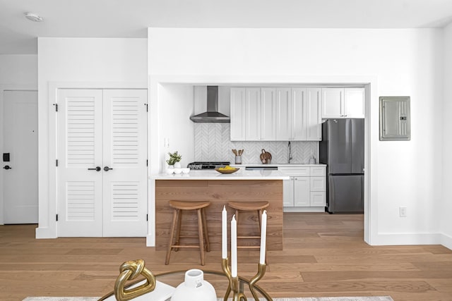127 Jane St, Weehawken, NJ 07086 - kitchen featuring freestanding refrigerator, wall chimney range hood, electric panel, light wood-style flooring, and light countertops