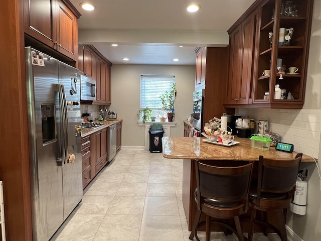 kitchen with stainless steel appliances, light stone counters, a kitchen breakfast bar, kitchen peninsula, and decorative backsplash