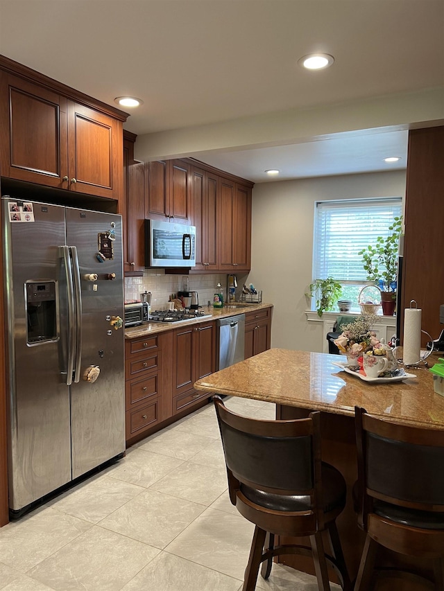 kitchen featuring stainless steel appliances, light stone counters, light tile patterned flooring, a kitchen breakfast bar, and tasteful backsplash