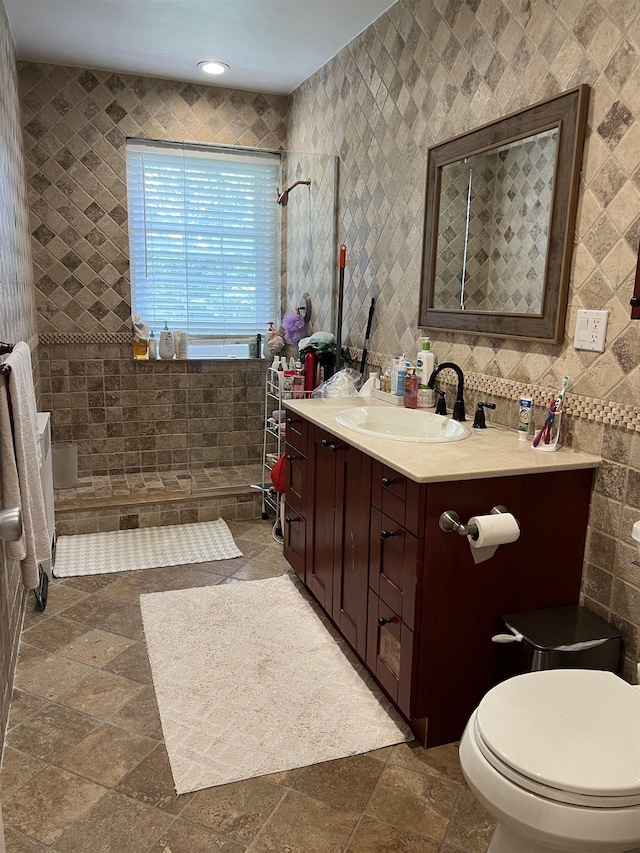 bathroom featuring toilet, tiled shower, tile walls, and vanity