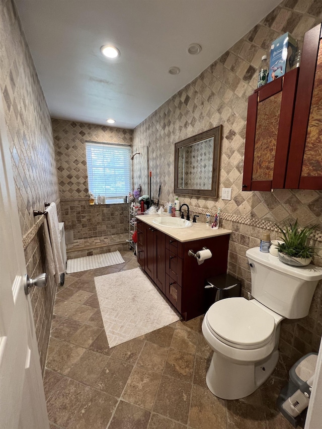 bathroom with tile walls, walk in shower, vanity, and toilet