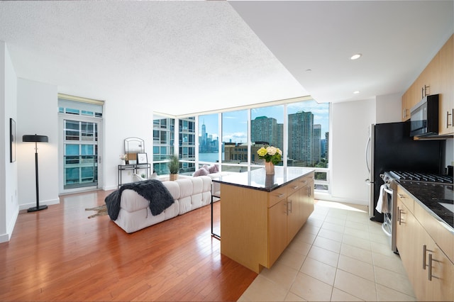 1 Shore Ln Unit 1208, Jersey City, NJ 07310 - kitchen featuring stainless steel range with gas cooktop, light brown cabinetry, a kitchen island, open floor plan, and light wood finished floors