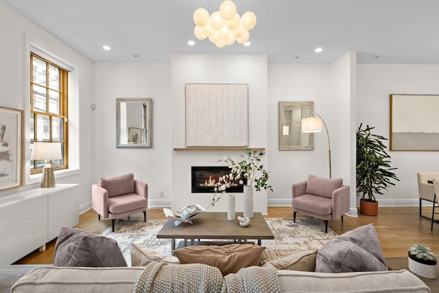 living area featuring a notable chandelier, a glass covered fireplace, wood finished floors, recessed lighting, and baseboards